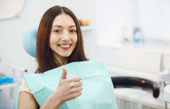 happy young woman in a dental chair showing her thumb up
